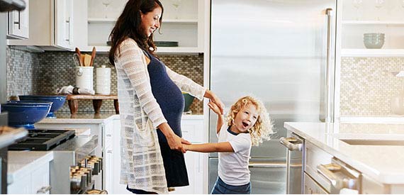 A pregnant mother and her son dancing in the kitchen.