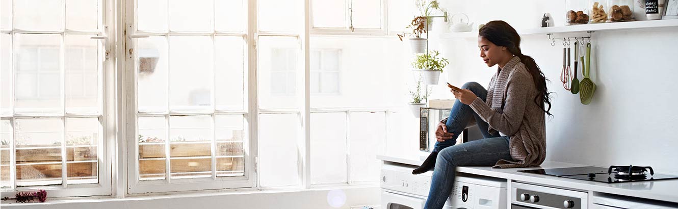 A woman sitting on her kitchen counter checking her smartphone.