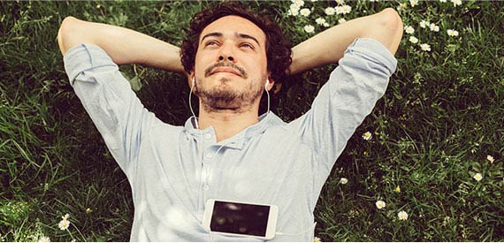 Man laying in the grass listening to music on his phone.