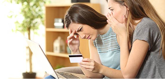 Two very worried women holding a car and looking at a computer screen.